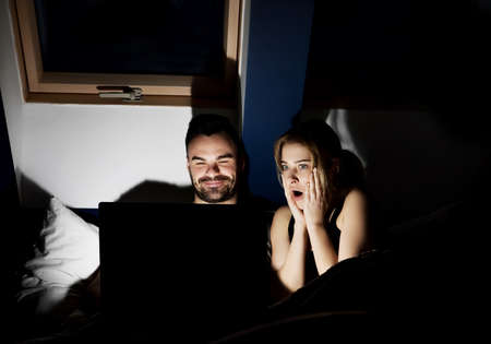 Young couple with laptop watching movie in bed.の写真素材