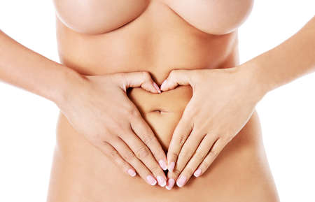 Closeup young woman making heart shape with her hands on her belly, isolated on white.の写真素材