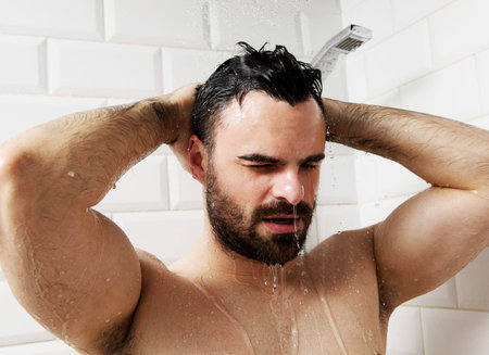 Handsome naked young man taking shower in bathroom