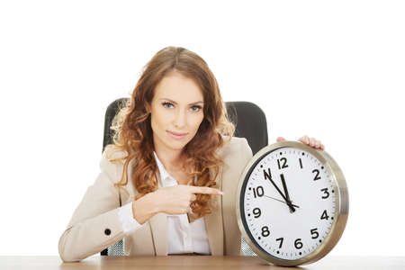 Businesswoman pointing on a clock by a desk.の写真素材
