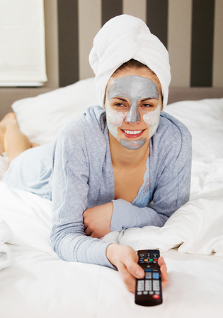 Young woman with clay mask on face watching tv at home.の写真素材