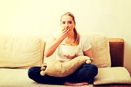 Young woman watching TV and eating chipsの写真素材