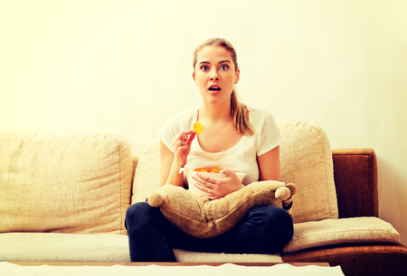 Young woman watching TV and eating chipsの写真素材