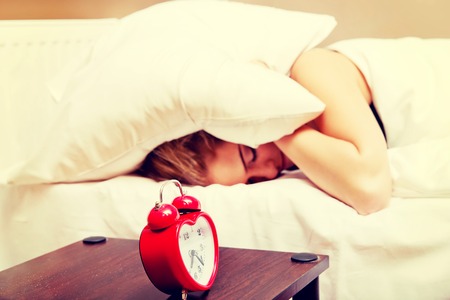 Young woman trying to sleep when alarm clock ringingの写真素材
