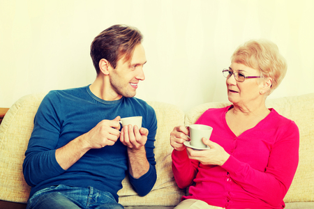 Mother and son sitting on couch and drinking tea or coffeeの写真素材