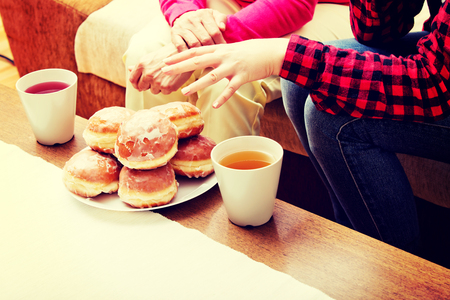 Mother and daughter sitting on couch with donuts and tea on tableの写真素材