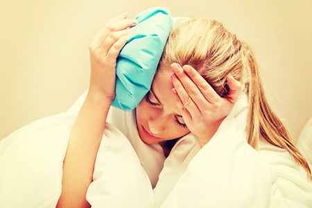 Young woman with headache, holding an ice-bag next to her forheadの写真素材