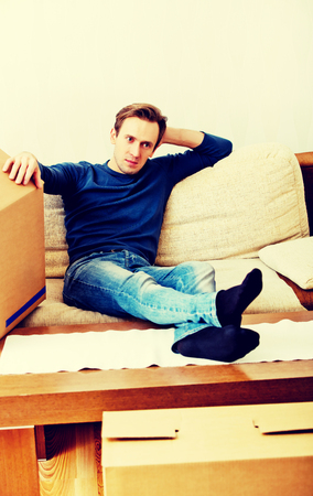 Tired man sitting on couch with cardboard boxes aroundの写真素材