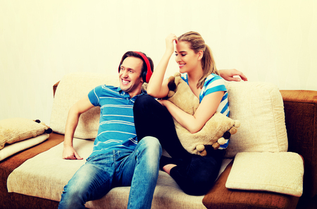 Couple relaxing on the sofa, man listening music woman hugging himの写真素材