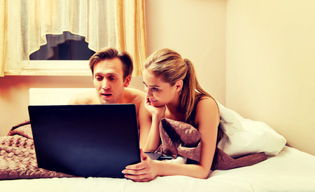 Young couple using laptop in bedの写真素材