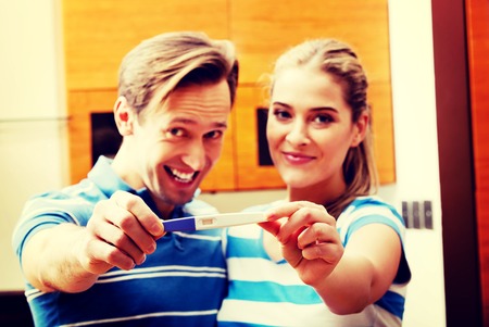 Young happy couple with pregnancy test standing in kitchenの写真素材