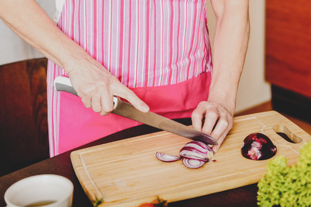 Female hands cutting bulb Edelweiss onionon wooden board, in kitchen.