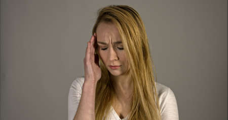 A young woman with a headache holding head, isolated on grey backgroundの写真素材