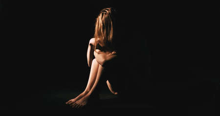 Nude woman in dark room. Abuse and depression concept.の写真素材