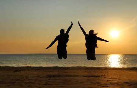 A silhouette of two young girls jumping at beachの写真素材