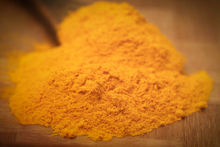 Ground turmeric in a spoon on wooden surface