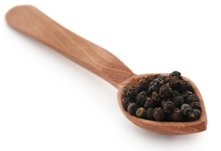 Black peppers on wooden spoon over white backgroundの写真素材