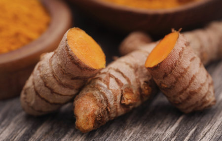 Raw turmeric with powder in a bowl on wooden surface