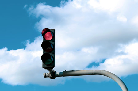 Red traffic light in street against blue sky with white cloud