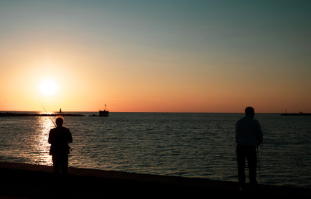 Silhouette of two anglers fishing at Malmo horbor at late afternoonの写真素材
