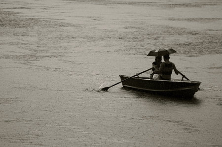 Black and white picture of woman that that keep's under her umbrella a man while rowing under heavy...