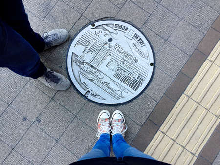 Kobe, Hyogo, Japan - 15th November 2018 : Female and Male legs wearing sneakers and standing in front of a beautifully decorated Manhole of Kobe City, Japanのeditorial素材