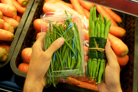 Beans bundled in a plastic package and other beans wrapped in Banana leaf held in female hands. This...