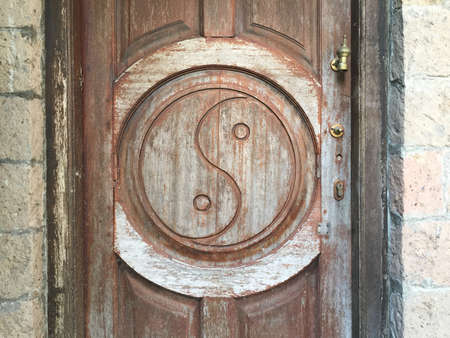 Yin-yang symbol beautifully carved on a wooden weathered doorの写真素材