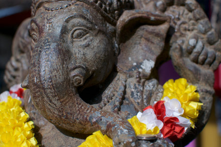 Side view of a beautiful small bronze Ganesha statue decorated with a colorful garland and located in Ubud, Bali - Indonesiaの写真素材