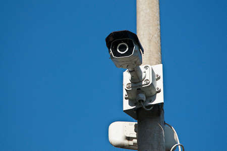 Close up picture of a CCTV surveillance security camera video installed on a street light pole with a blue sky in the background and located in Caslano, Ticino - Switzerlandの写真素材