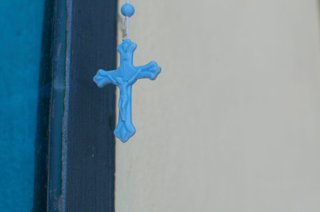 Small blue necklace cross hanging in front of a colorful wall. This is a symbol of hope and...