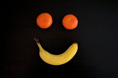A smiling grimace made out with tangerines and a banana on a black background. This can be used for conceptual photo as happiness, positivity and cheerfulnessの写真素材
