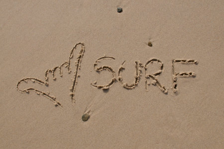 Shaka hand gesture and surf text inscription drawn in the sandの写真素材