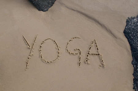 Yoga inscription handwritten on the sand and framed with black rocksの写真素材