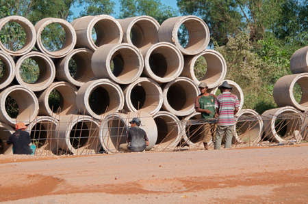 Sihanoukville, Cambodia - 30th December 2018 : View of a cambodian road construction site with workers on the street and many drainage concrete pipes piled in the backgroundのeditorial素材