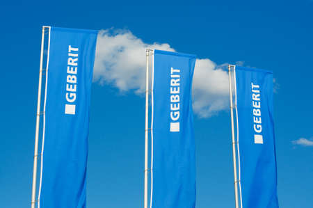 Manno, Switzerland - 18th March 2021 : View of three Geberit company flags against blue sky in Switzerland. Geberit is a Swiss multinational specialized in manufacturing and supplying sanitary partsのeditorial素材
