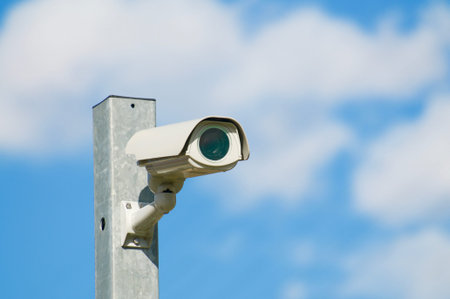 CCTV surveillance security camera video installed on a iron pole with a blue sky and clouds in the...