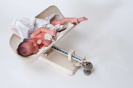 Neborn baby in a vintage scale being weighedの写真素材