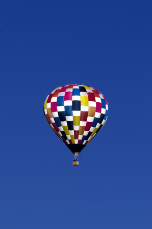 a vivid multicolored hot air balloon is isolated against a crisp blue skyの写真素材