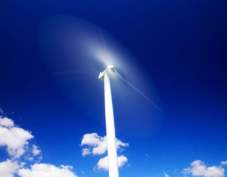 Wind turbine in motion against a regal dark blue sky guarded below by splendid white clouds.