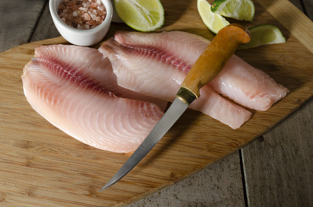 raw tilapia fillets on cutting boardの写真素材