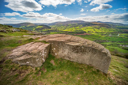 View over Usk valley to Brecon Beacons from Allt yr esgair hillside. Large rock with rippled pattern in foreground. Wales, UK. Aprilの写真素材