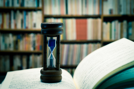 Hourglass against book shelfの写真素材