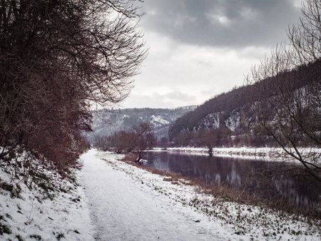 White footpath full of snow and without people. On one sight rocky hill and on the other slowly...