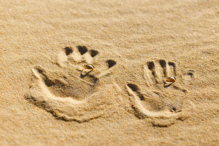 Two palm prints on the sand with wedding rings.の写真素材