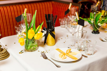 Birthday guests table setting with fresh flowers in black and gold style, indoor.