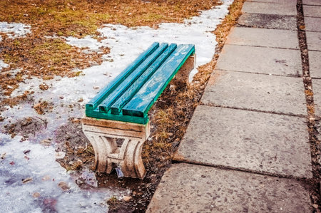 Bench in the old abandoned park. Early springtime and ground covered the snow.