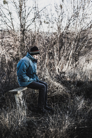 A young man sits on an old bench in the countryside in the autumn timeの写真素材