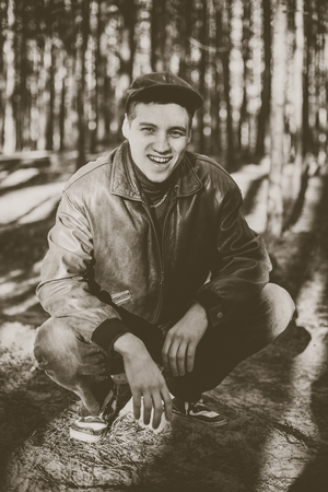 A guy in a leather jacket and cap sits on a road in a pine forestの写真素材
