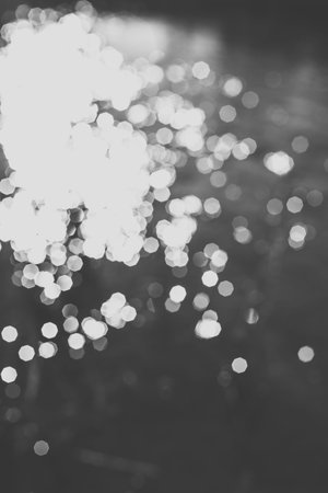 Blur bokeh background of water with flecks of sunlight. Monochrome photo